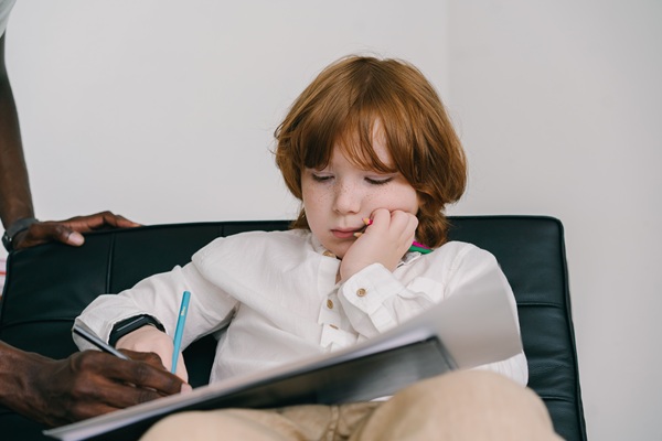 A young boy with red hair concentrating on drawing